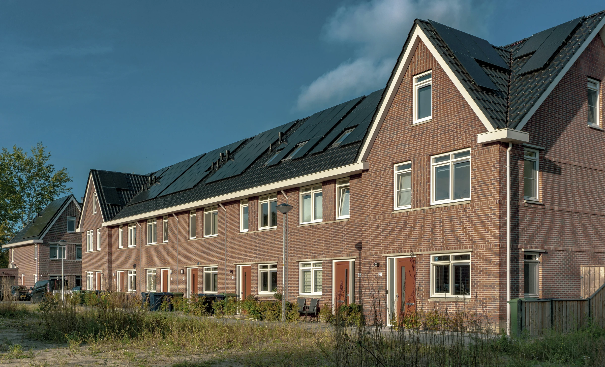 Een rij bakstenen woningen met donkere daken en zonnepanelen