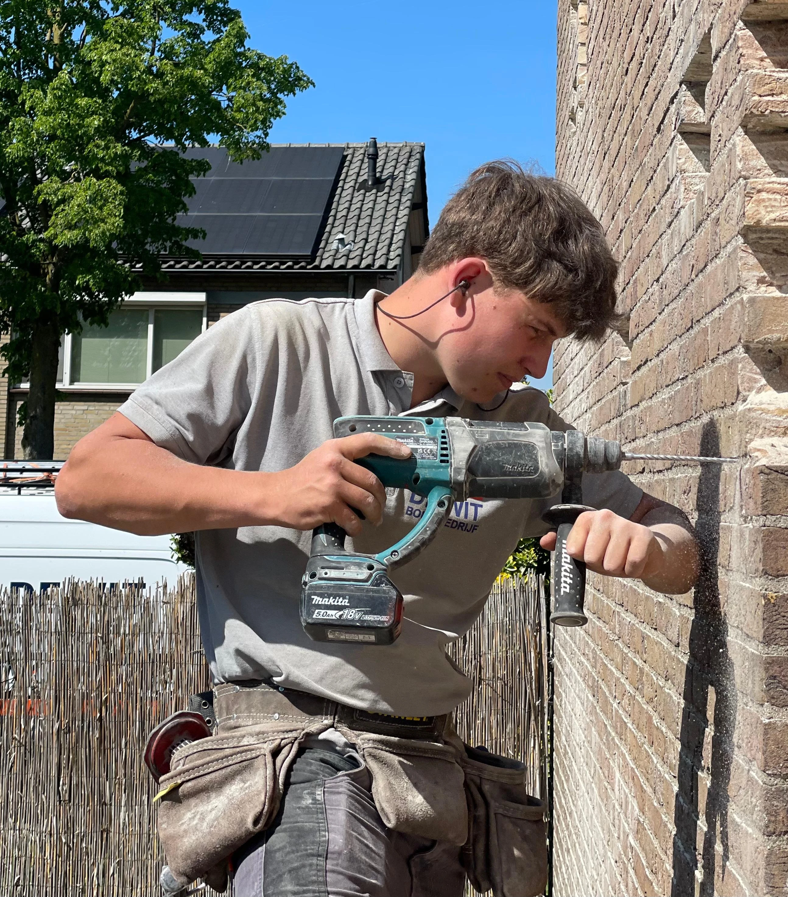 Een medewerker van De Wit Bouwbedrijf boort in een gemetselde gevel